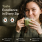 A woman with curly hair holds a clear glass mug filled with a light green beverage, smiling at the camera. Large text on the left reads 'Taste Excellence in Every Sip,' with circular icons for 'Minimal Bitterness' and 'Creamy Finish,' plus feature callouts at the bottom.