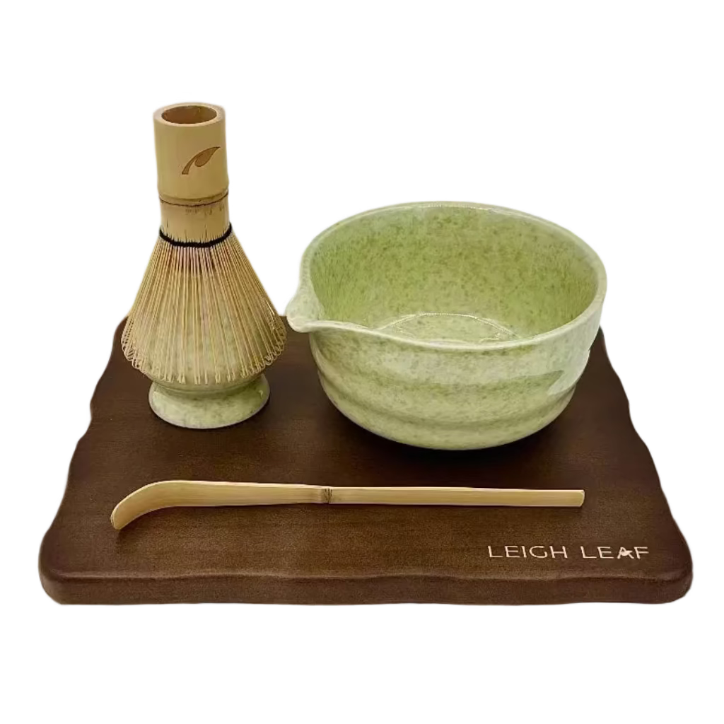 Discover the beauty of the 5 Piece Matcha Whisk Set with Wooden Display Board from Leigh Leaf, showcasing a green matcha bowl, bamboo whisk, and a wooden base for a refined tea experience.