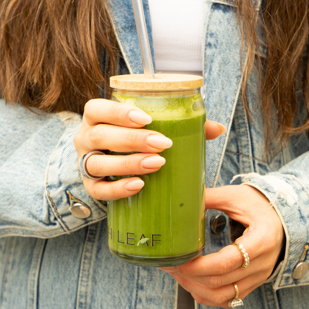 A woman holding a Leigh Leaf Elegant 16oz Matcha Sipper Glass filled with green matcha drink. The glass features a bamboo lid and straw, ideal for matcha glass sipper lovers.